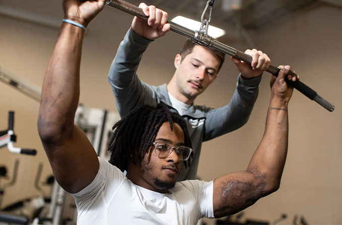 A student coaching another student on proper exercise form