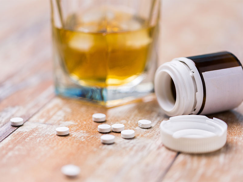 A glass of alcohol and a bottle of pills sitting on a table