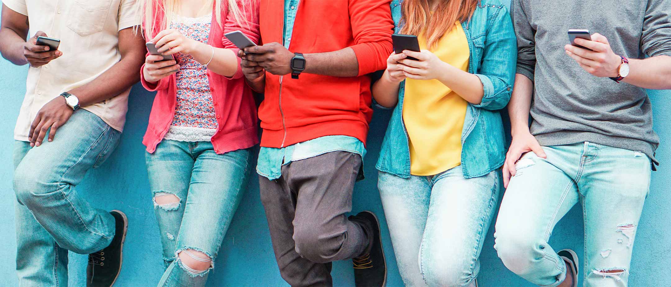 Students leaning against a wall viewing their phones