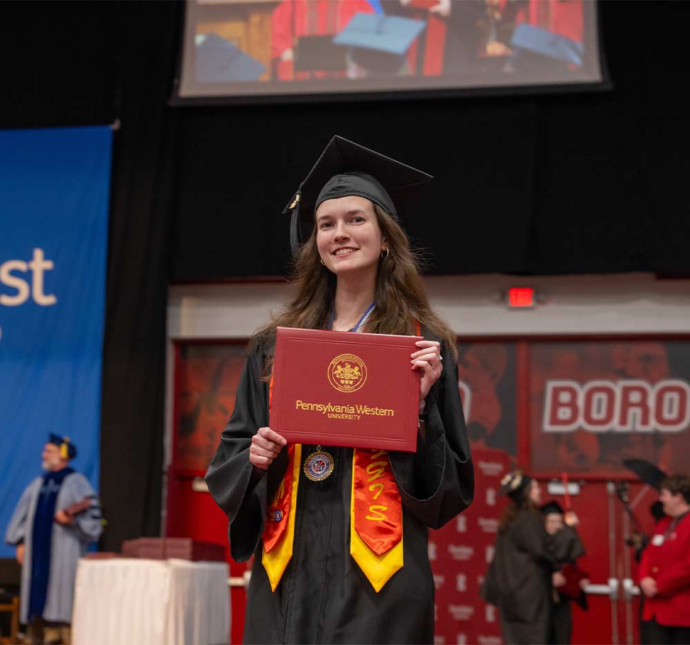 PennWest student celebrating graduation while holding a diploma cover, representing academic pathways, career readiness, workforce preparation, and student success.