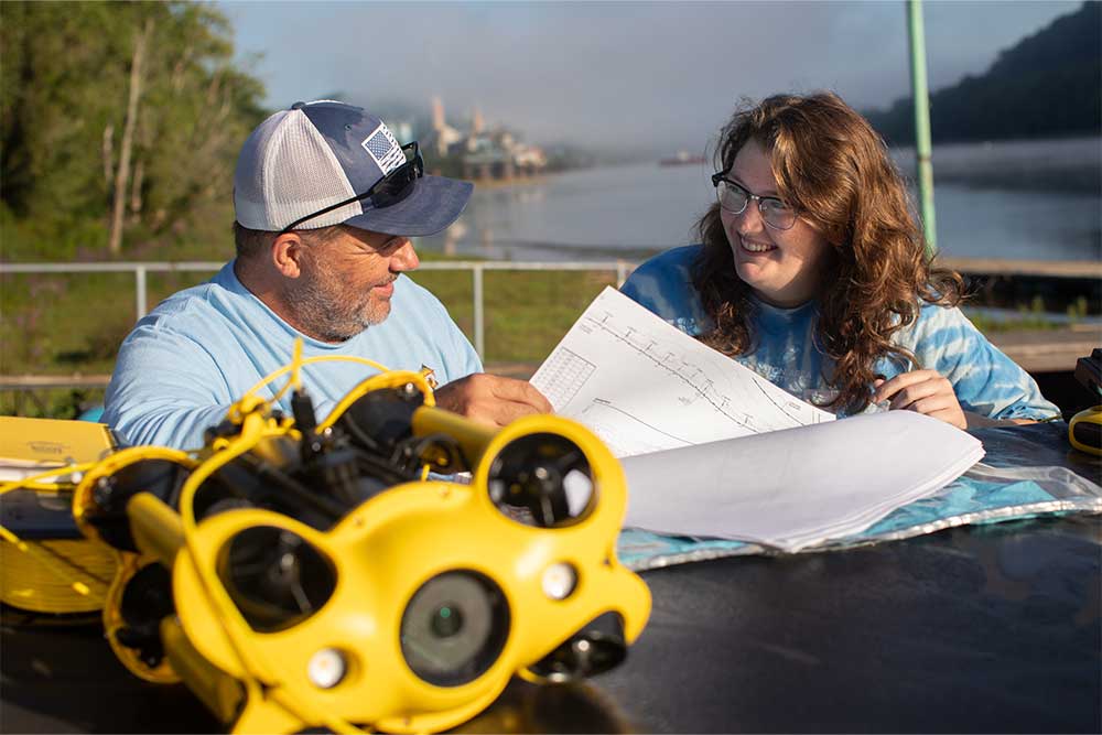 PennWest student and faculty member review environmental research data during a community-engaged learning project using underwater robotics equipment.