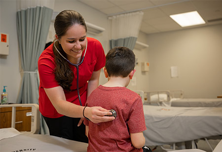 A nursing student listening to the heart of a patient