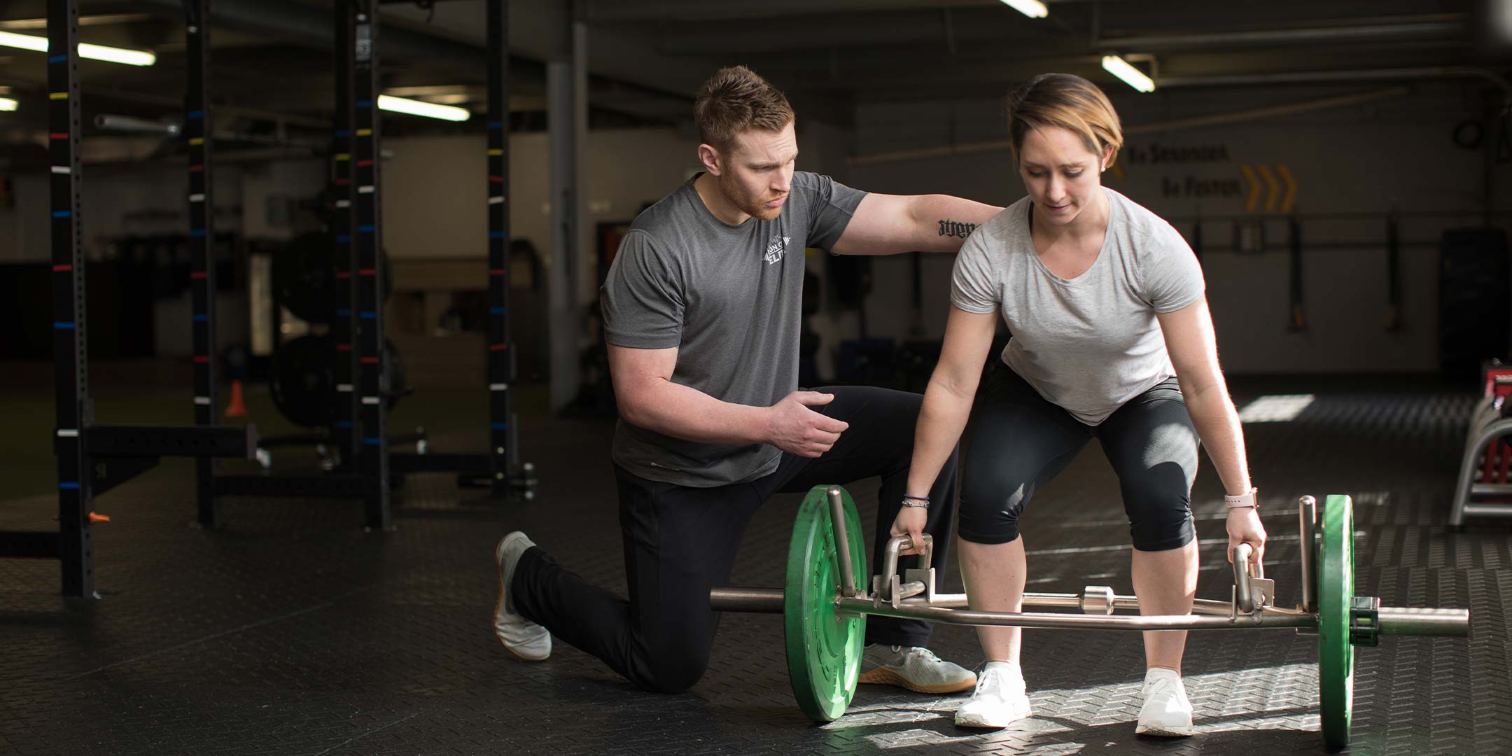 A conditioning coach instructing a student on proper deadlifting technique