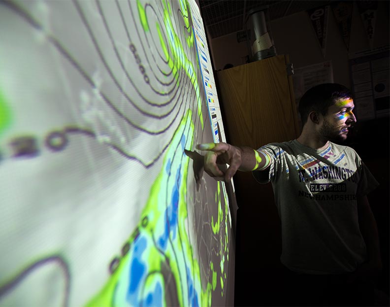 a climate variability and impacts student pointing at a weather pattern image on a projection screen