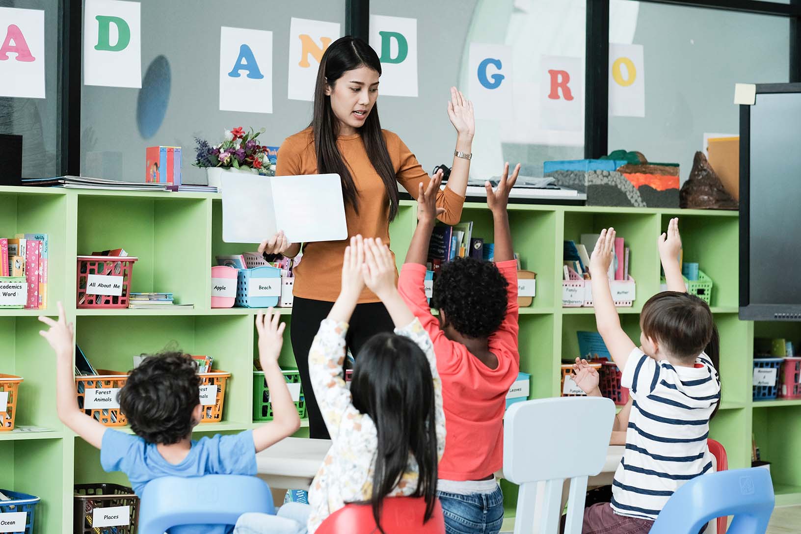 teacher in a classroom of students raising their hands
